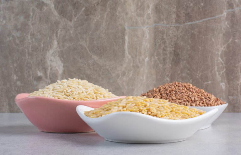 Portions of rice and buckwheat sorted in bowls on marble background
