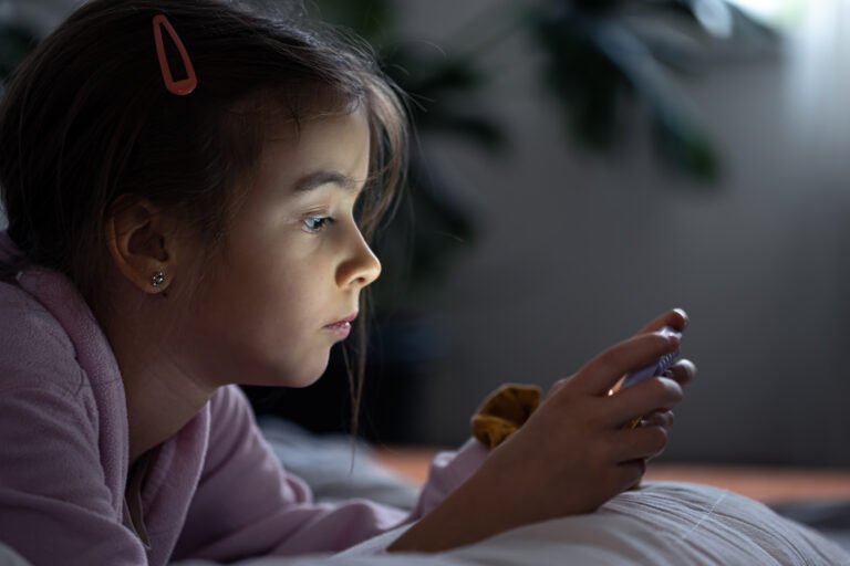 Little girl uses a smartphone lying on the pillow at home