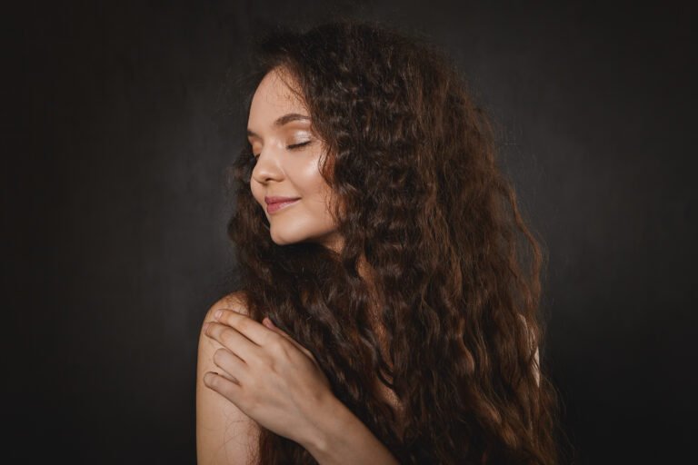 Isolated studio shot of gorgeous young European female model with neat make up and glowing skin wearing her beautiful dark hair loose, looking away with joyful smile, keeping her eyes closed