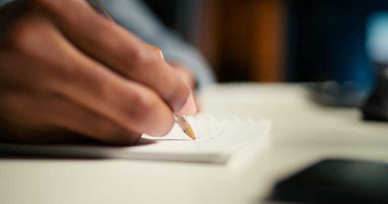 Black freelancer researching online data and writing notes for articles